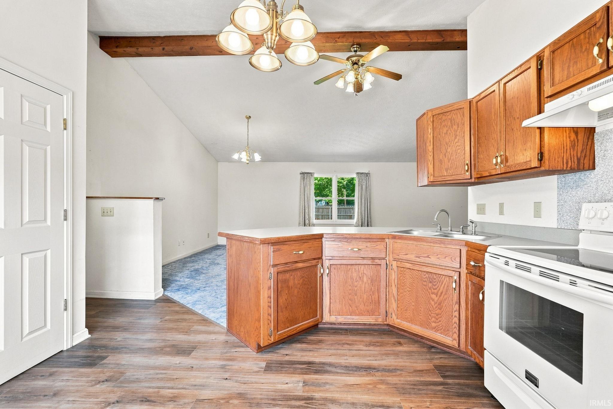 Kitchen featuring wood-finish flooring, wood cabinetry with gold-tone hardware, a white range, and a dual-basin sink