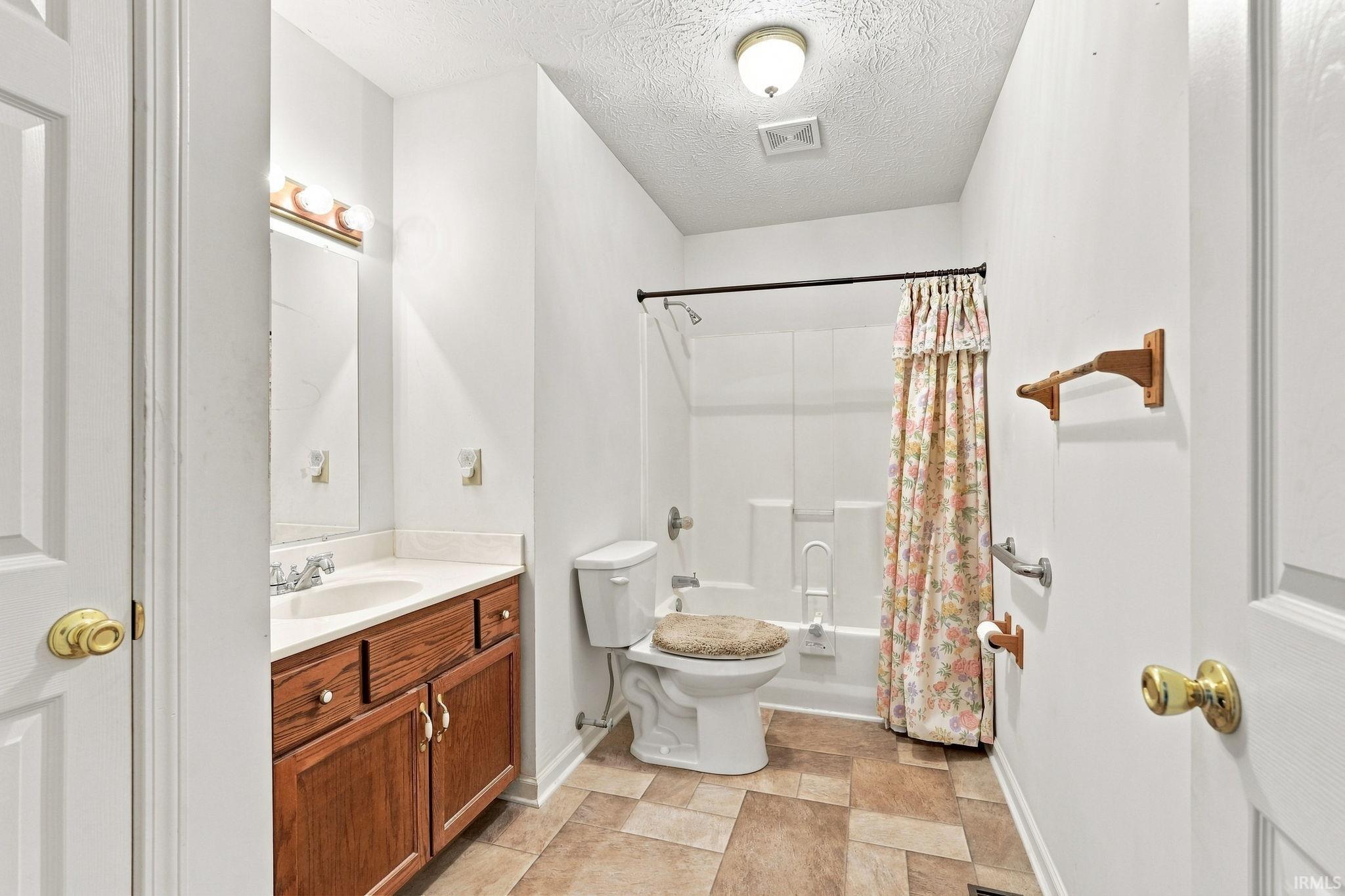 Bathroom featuring a wood-finish vanity with a single basin, combination shower and tub, and patterned floor tiling