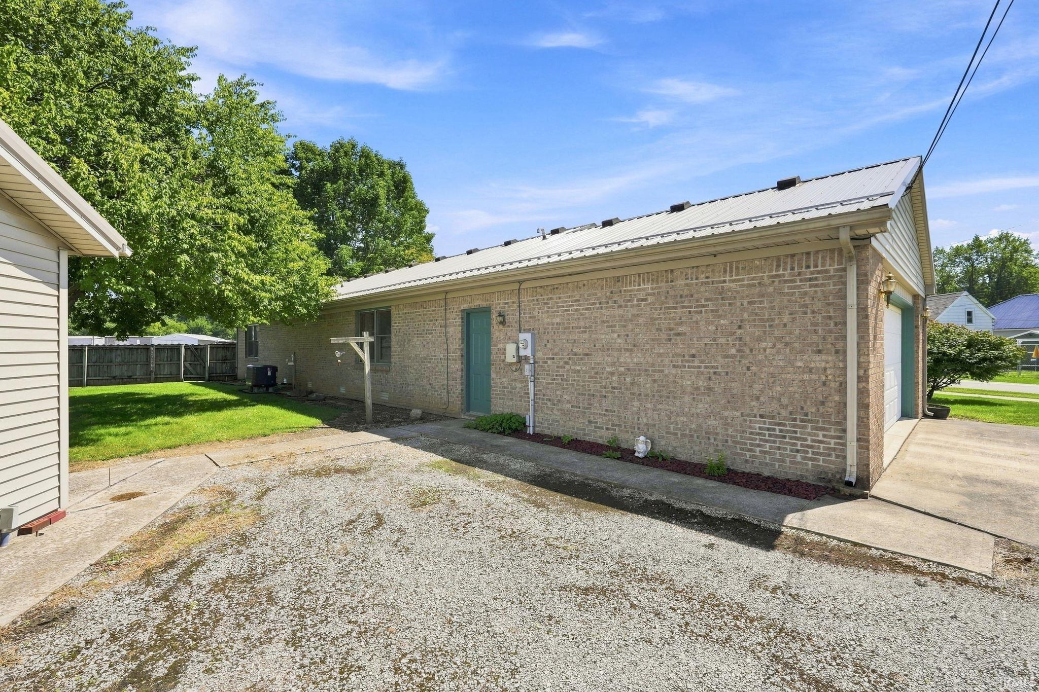 Brick exterior with a metal roof, an attached garage, a gravel driveway, and a separate outbuilding