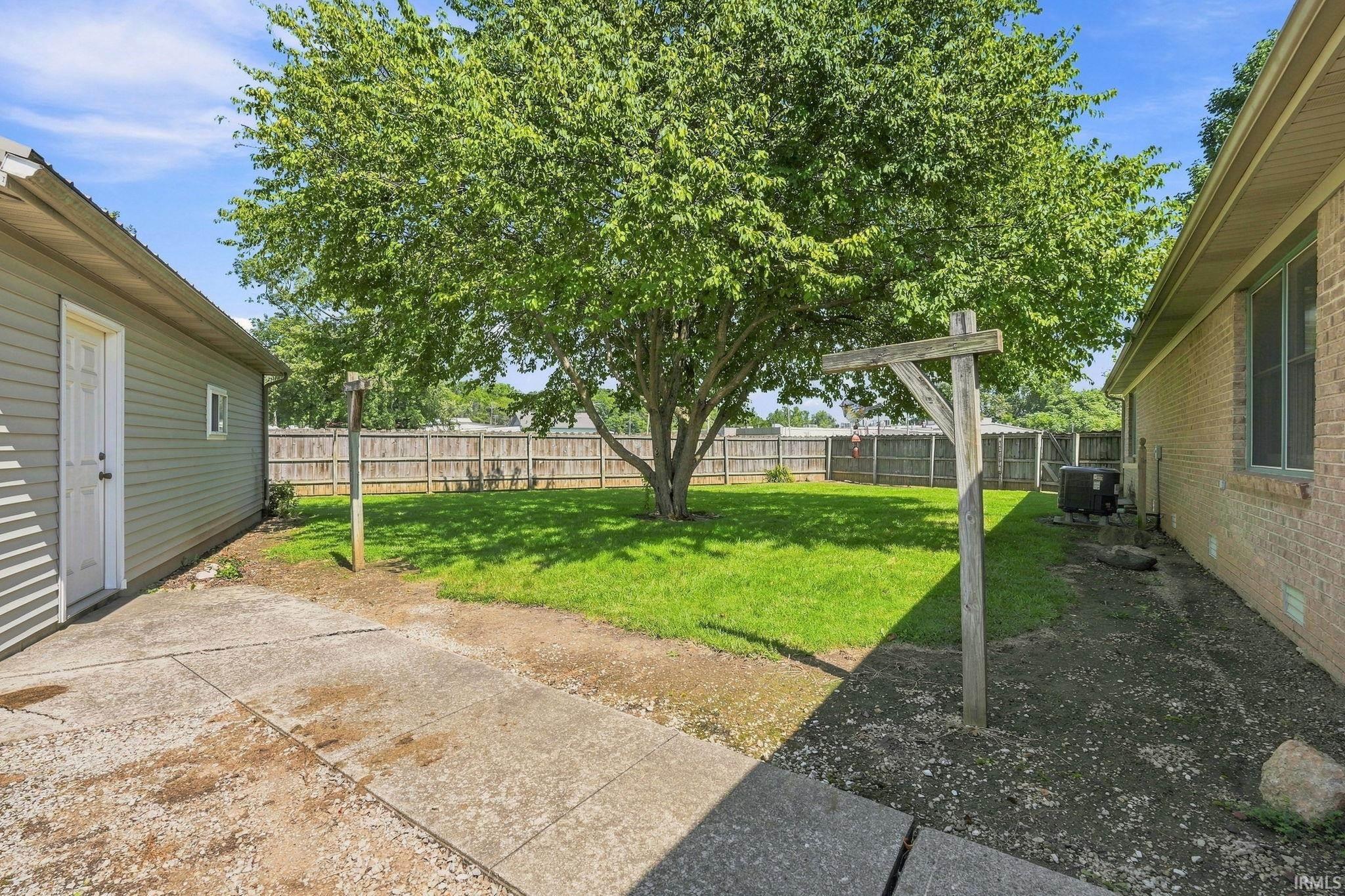 Expansive backyard featuring a mature tree, concrete patio, and wood privacy fencing