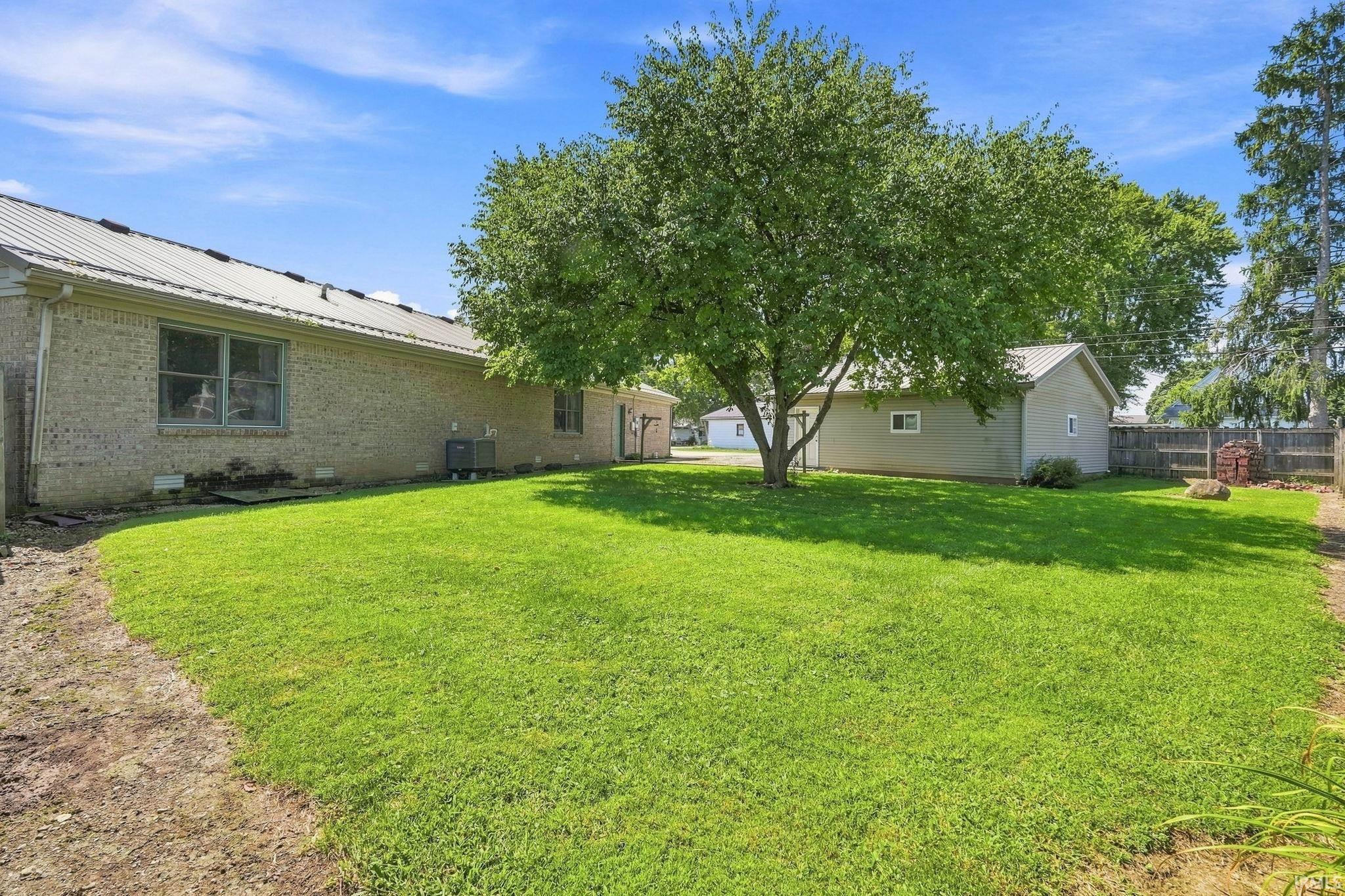 Expansive rear yard featuring green lawn, mature tree, and a detached structure with a metal roof