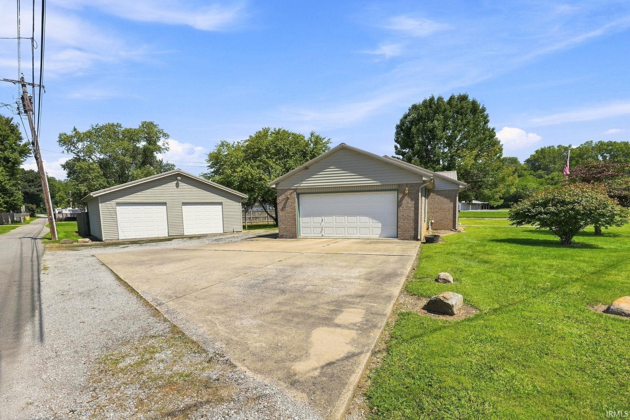Two-car attached garage with brick and siding exterior, two-car detached garage with siding exterior, concrete driveway, and expansive lawn area