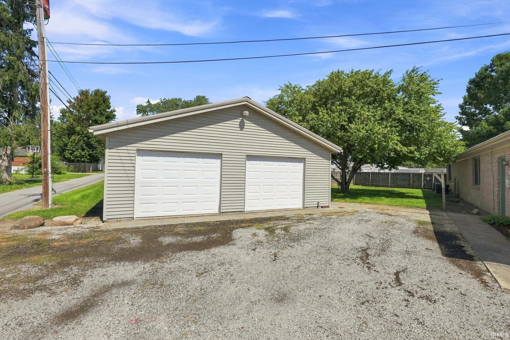 Detached two-car garage with white paneled doors, light-colored siding, and a gravel driveway
