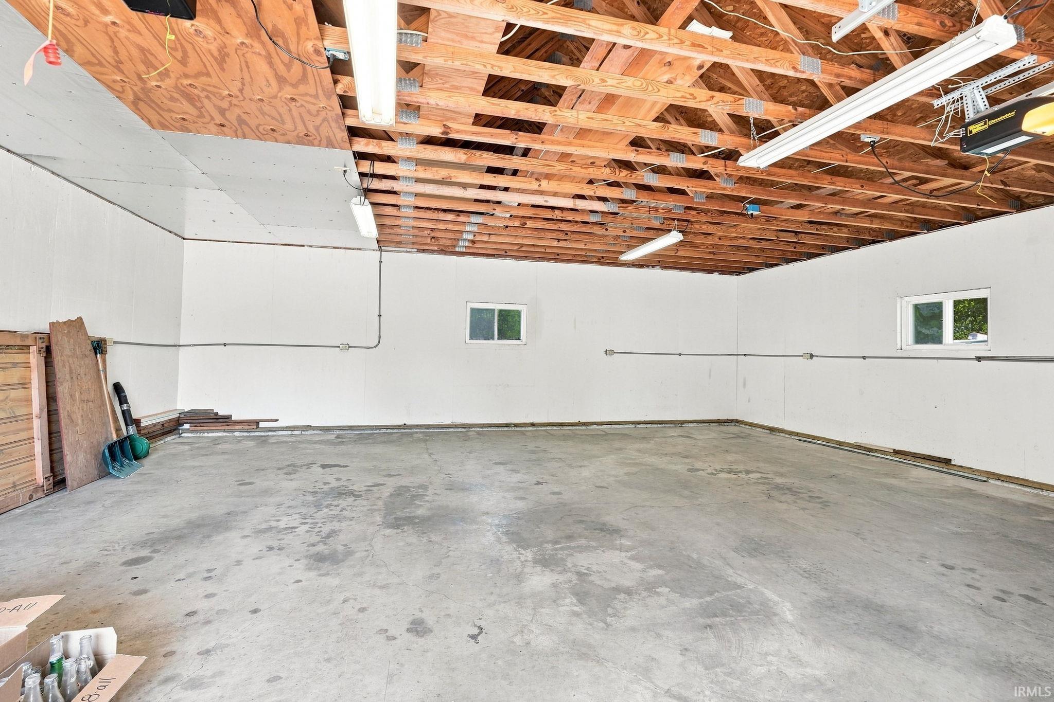 Concrete flooring with exposed wood joist ceiling, featuring two windows and fluorescent lighting