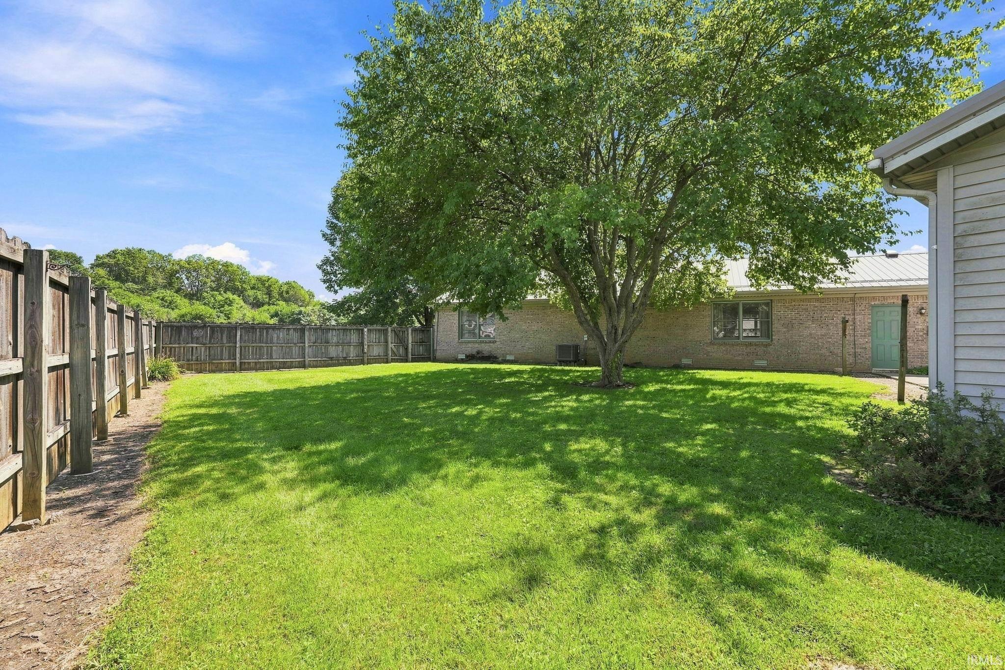 Expansive green lawn with mature tree, bordered by a privacy fence
