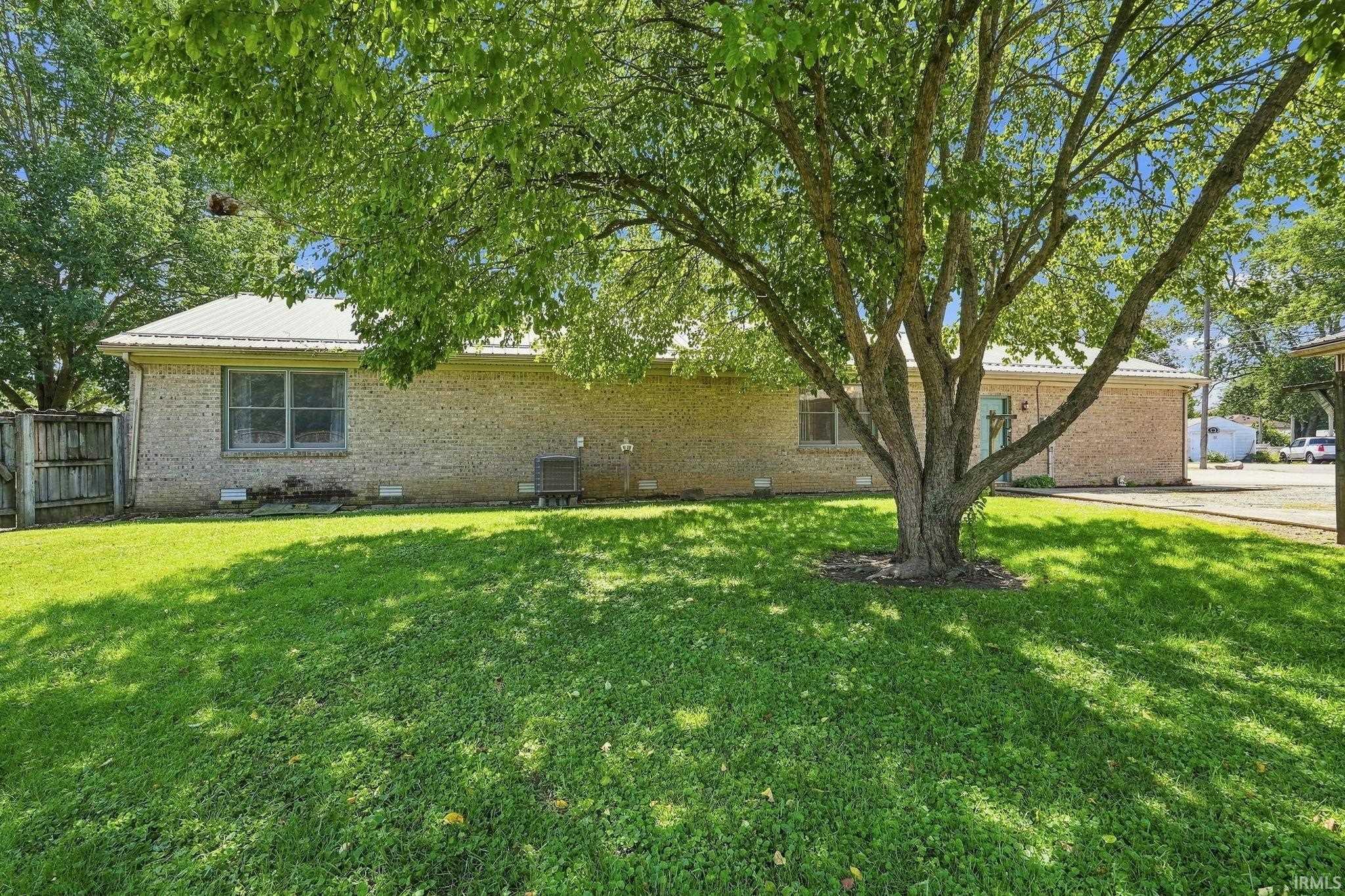Brick exterior with a metal roof, featuring a mature shade tree and green lawn