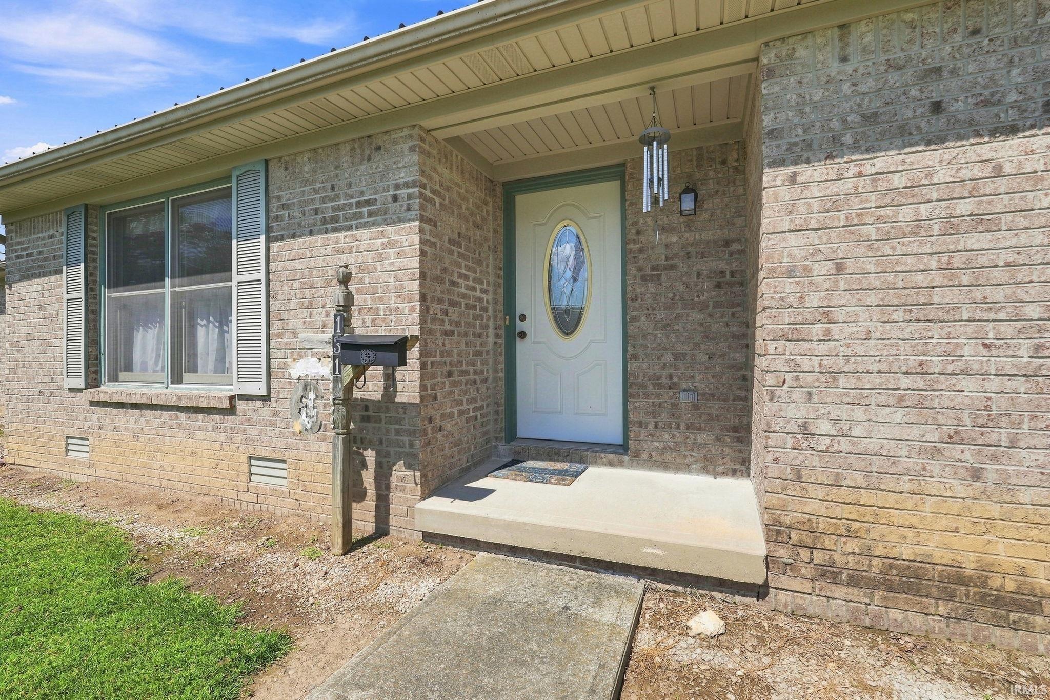 Brick exterior with window shutters, concrete porch, and a white front door with an oval glass insert
