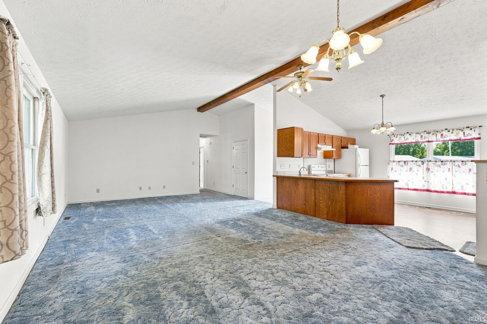 Vaulted ceiling with exposed beam, kitchen island with wood cabinetry, and a ceiling fan with integrated lighting