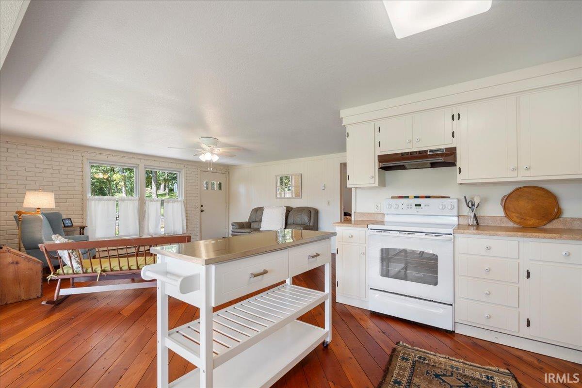 Wood-finish flooring throughout, white cabinetry with a light-toned countertop, and a white freestanding range