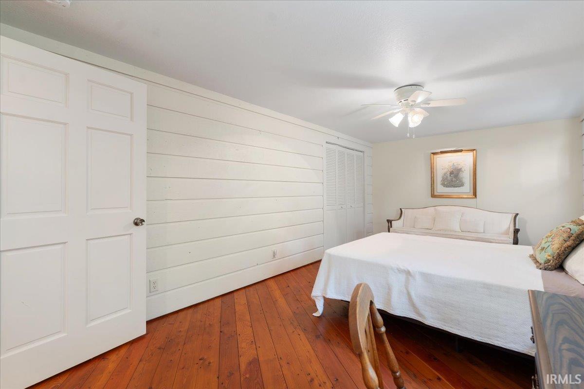 Wood-finish flooring, white paneled walls, ceiling fan, and white paneled doors