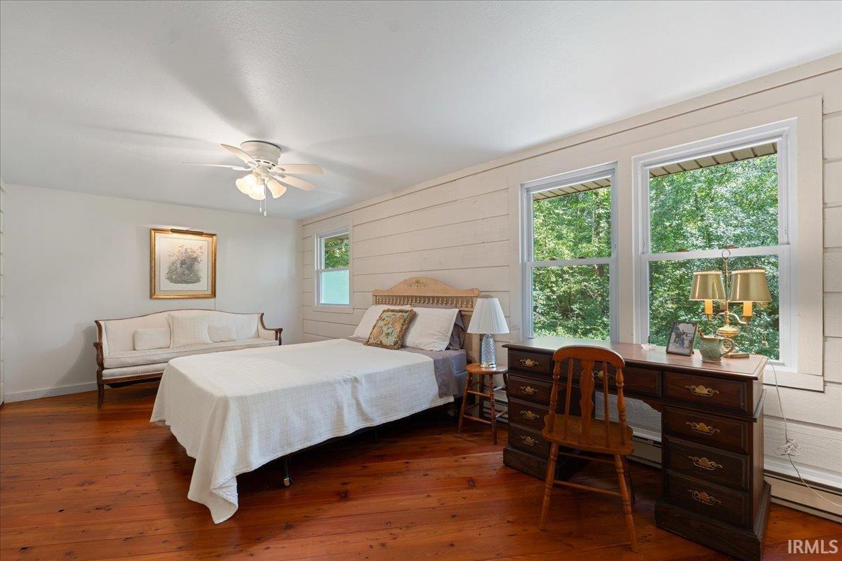 Wood-finish flooring, white shiplap wall accent, multiple windows providing natural light, and a ceiling fan with integrated lighting