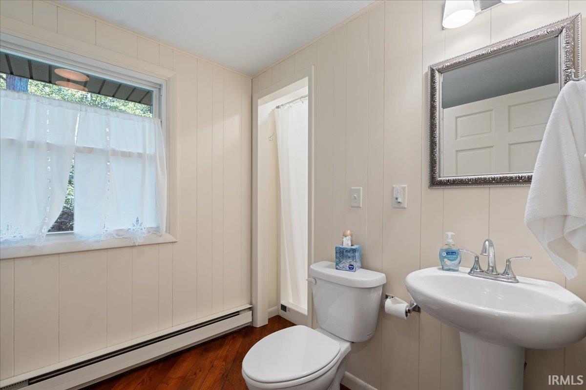 Pedestal sink with chrome-finish faucet, framed mirror, vertical panel wall treatment, and wood-finish flooring