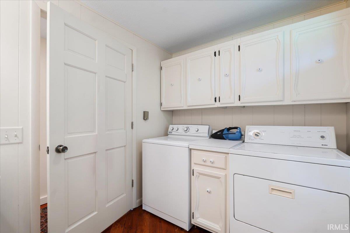 Laundry area featuring overhead cabinetry, paneling, and wood-finish flooring