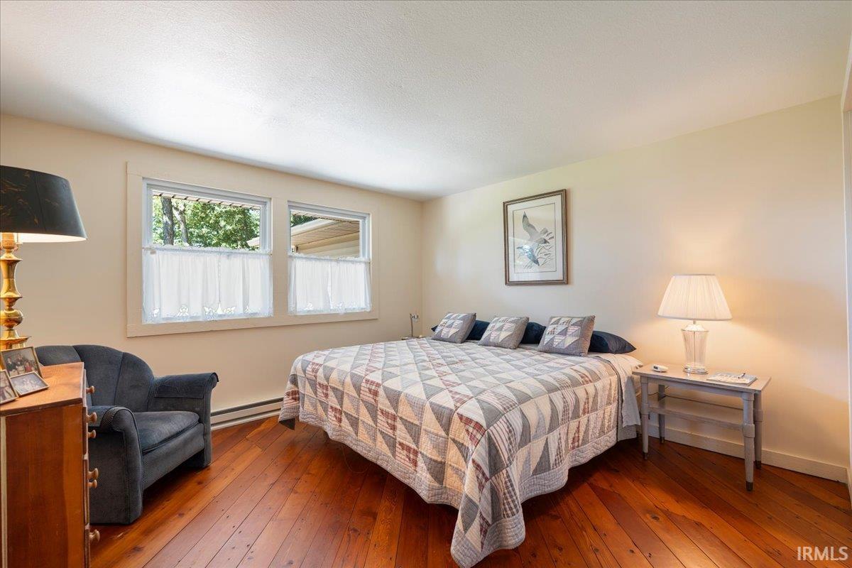 Hardwood flooring, painted walls, two windows, and a built-in baseboard heater