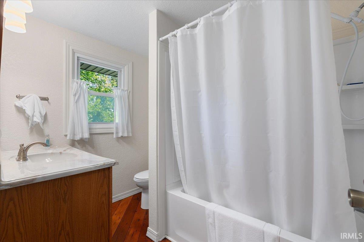 Bathroom featuring a wood-finish vanity with a single basin sink and brushed nickel faucet, a window with natural light, and a tub with a shower