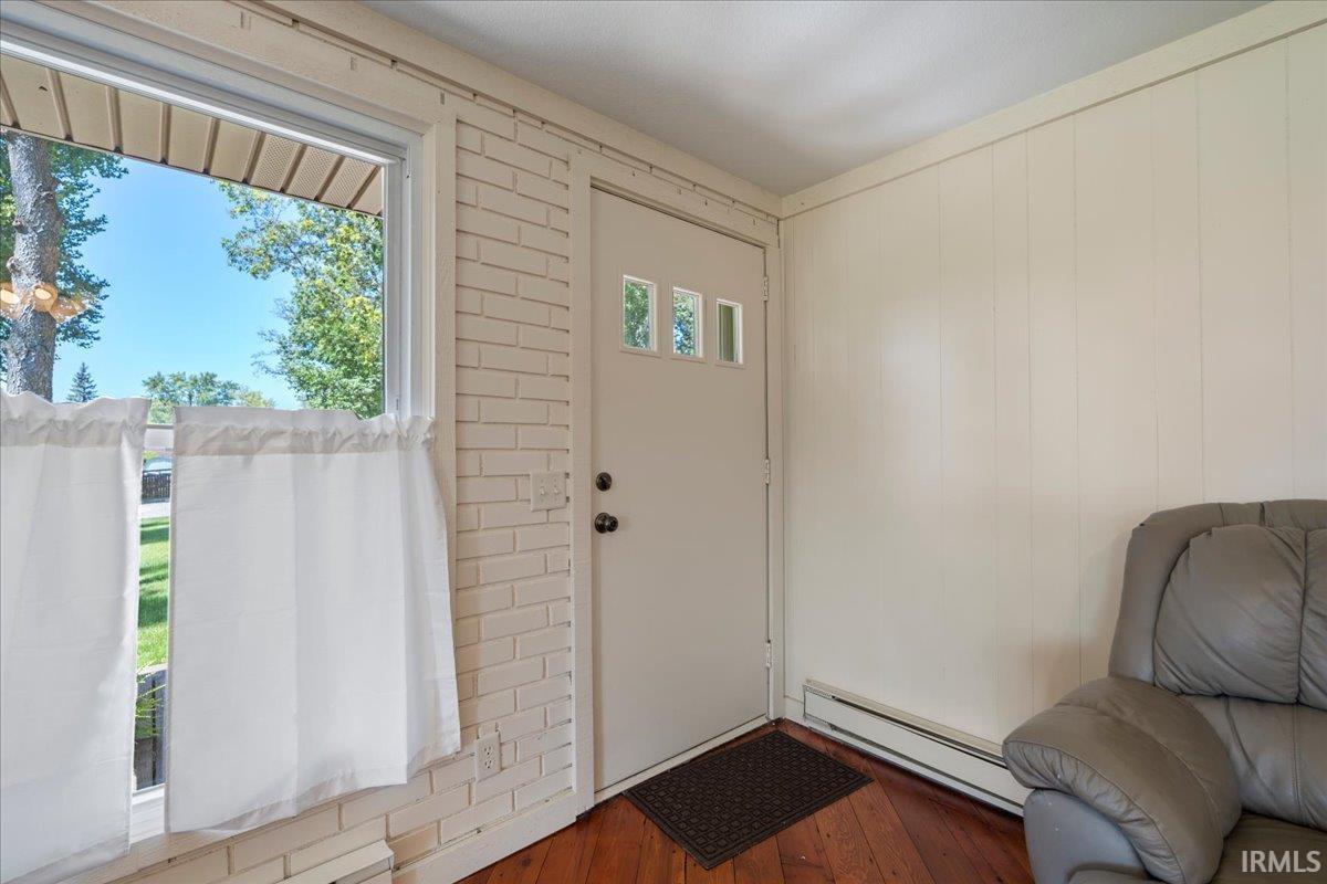 Entryway featuring wood-finish flooring, a white brick-patterned wall, and a solid door with three rectangular lites