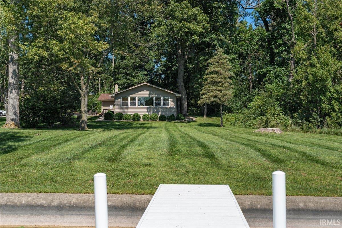Expansive green lawn with striped mowing pattern, bordered by mature trees and shrubs, leading to a white dock