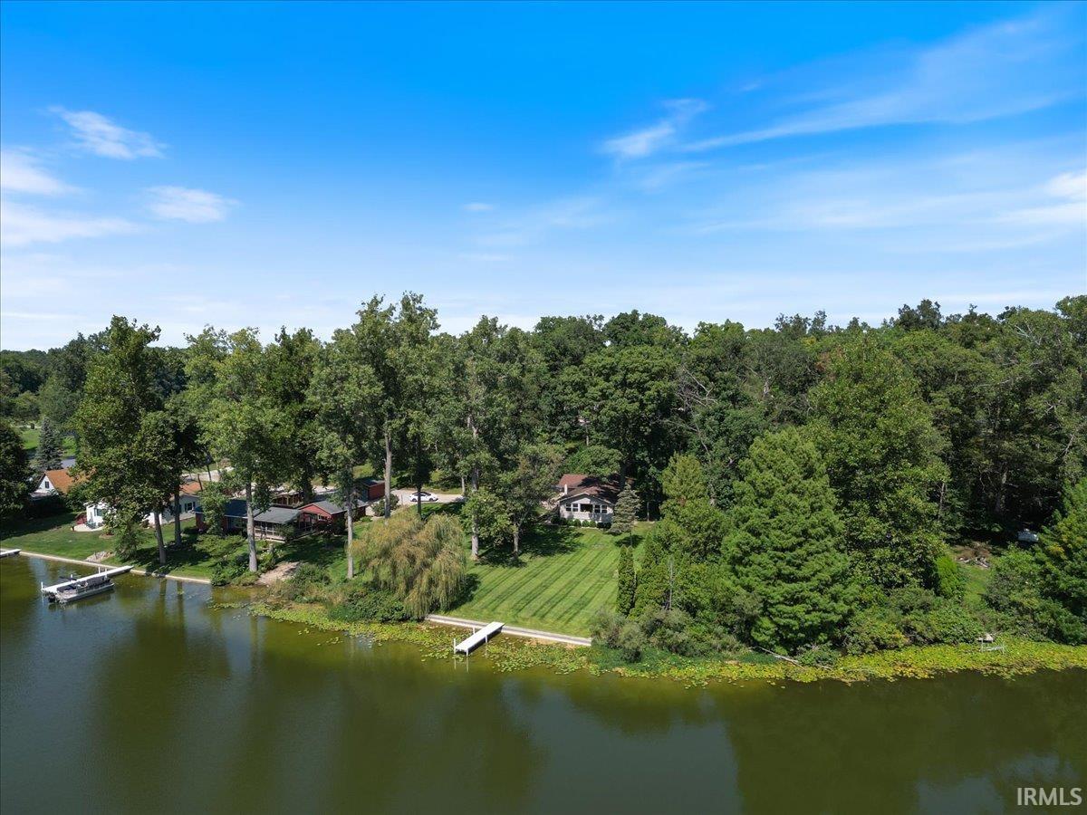 Waterfront property featuring a private dock, expansive green lawn, mature trees, and a residential structure