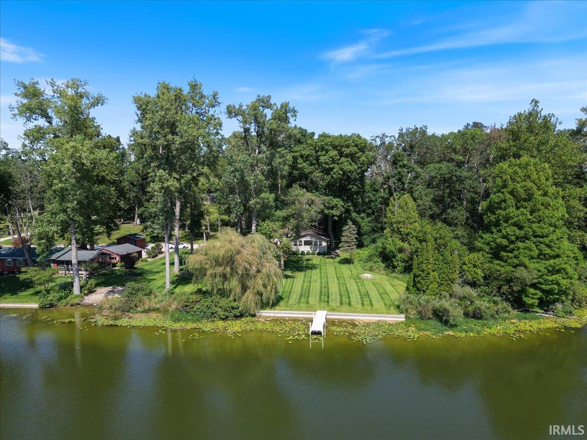 Expansive waterfront property featuring a private dock, lush green lawn, mature trees, and a secluded residence