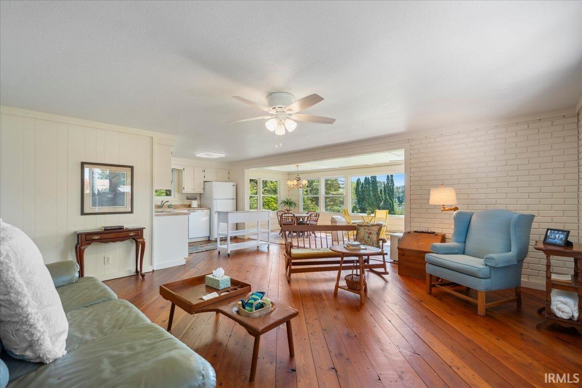 Hardwood flooring, painted brick accent wall, white paneled walls, ceiling fan, and recessed lighting