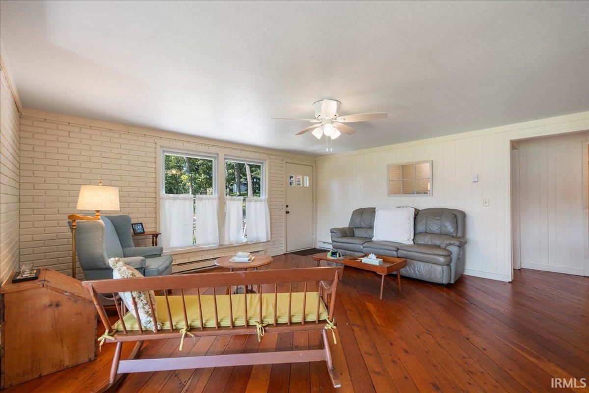 Brick accent wall, multiple windows, wood-finish flooring, ceiling fan, and paneled walls