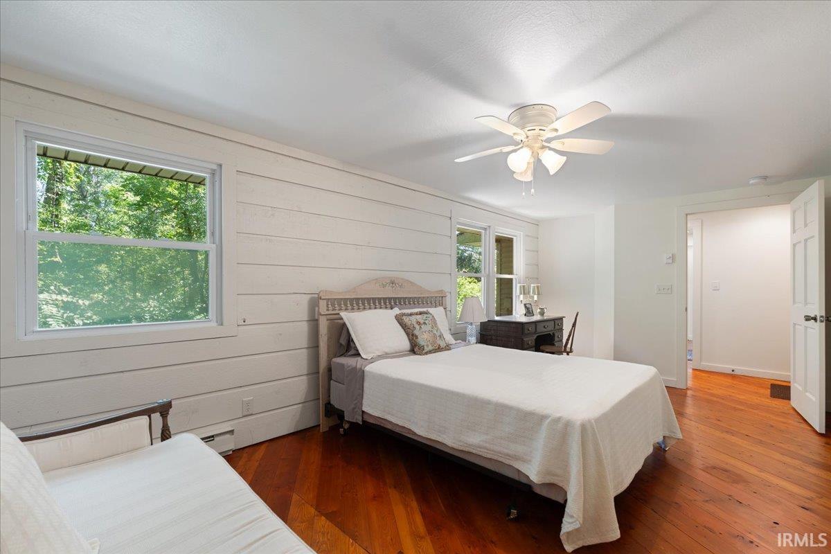 Hardwood flooring, painted shiplap wall, ceiling fan with integrated lighting, white trim windows, and white interior doors
