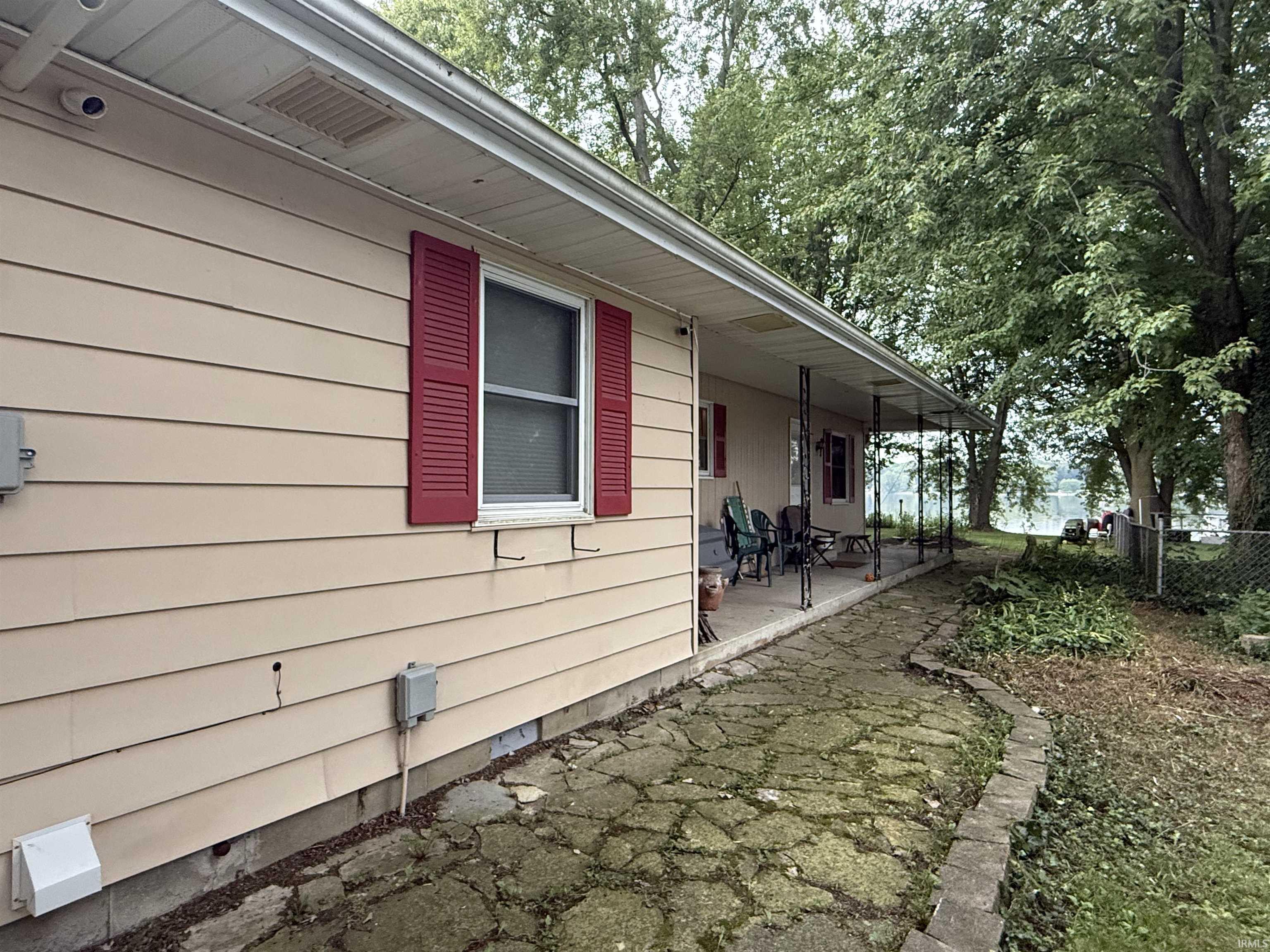 Single-story residence featuring horizontal siding, red louvered shutters, and a covered concrete porch with wrought iron columns