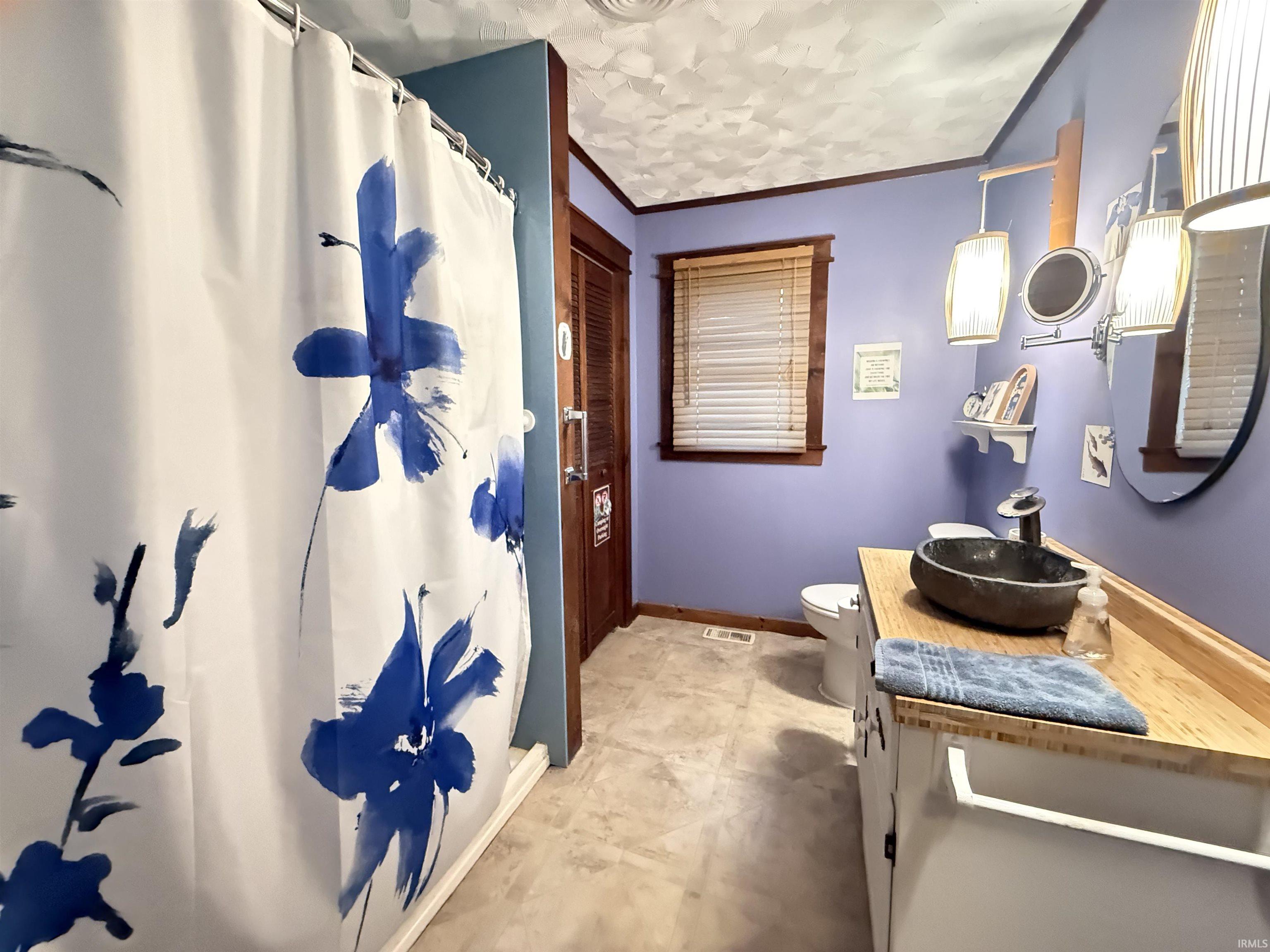 Bathroom featuring a vessel sink, wood-finish countertop, white vanity cabinetry, and a window with blinds