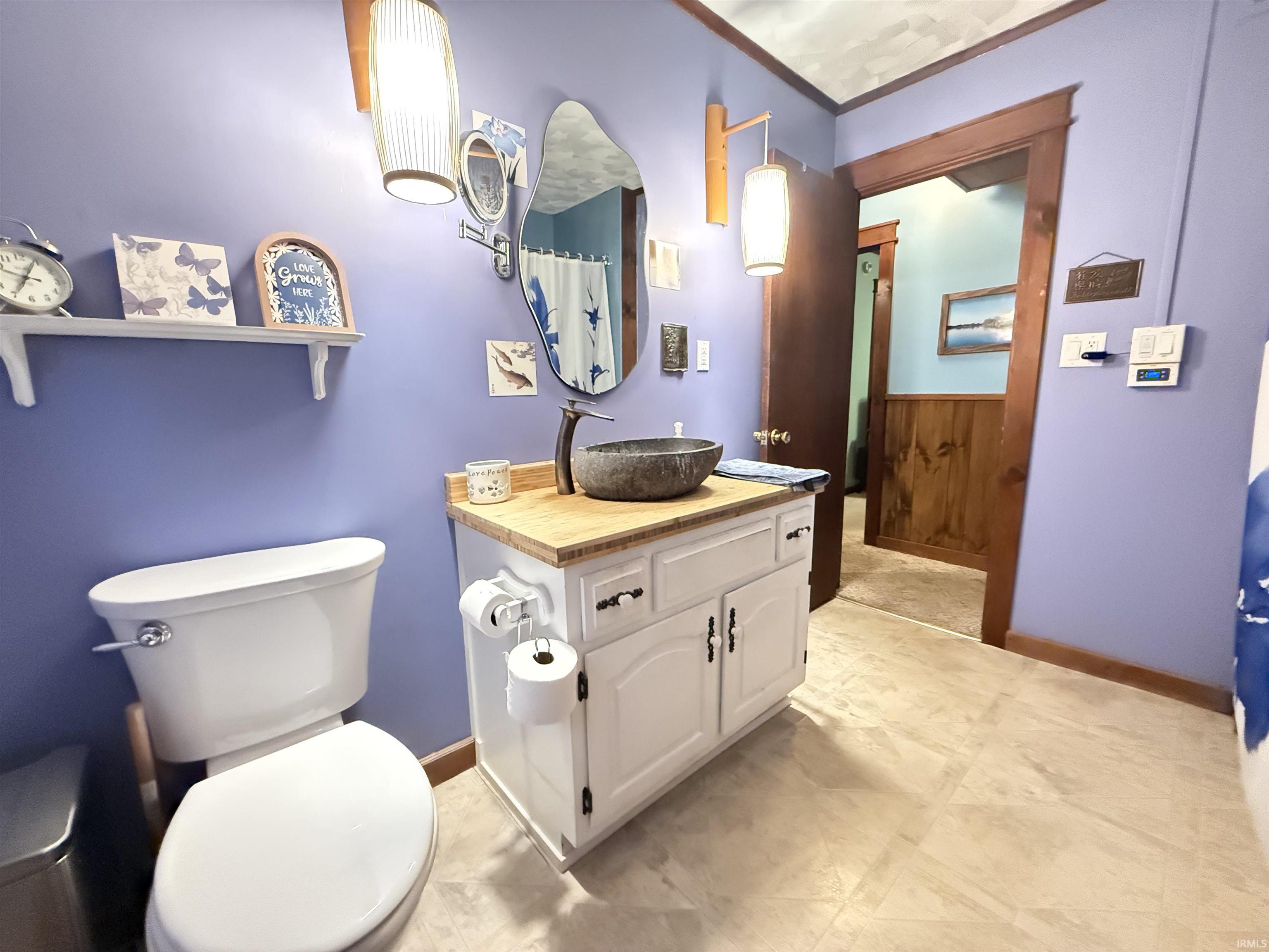 White vanity with a wood-finish countertop and vessel sink, complemented by a wall-mounted mirror
