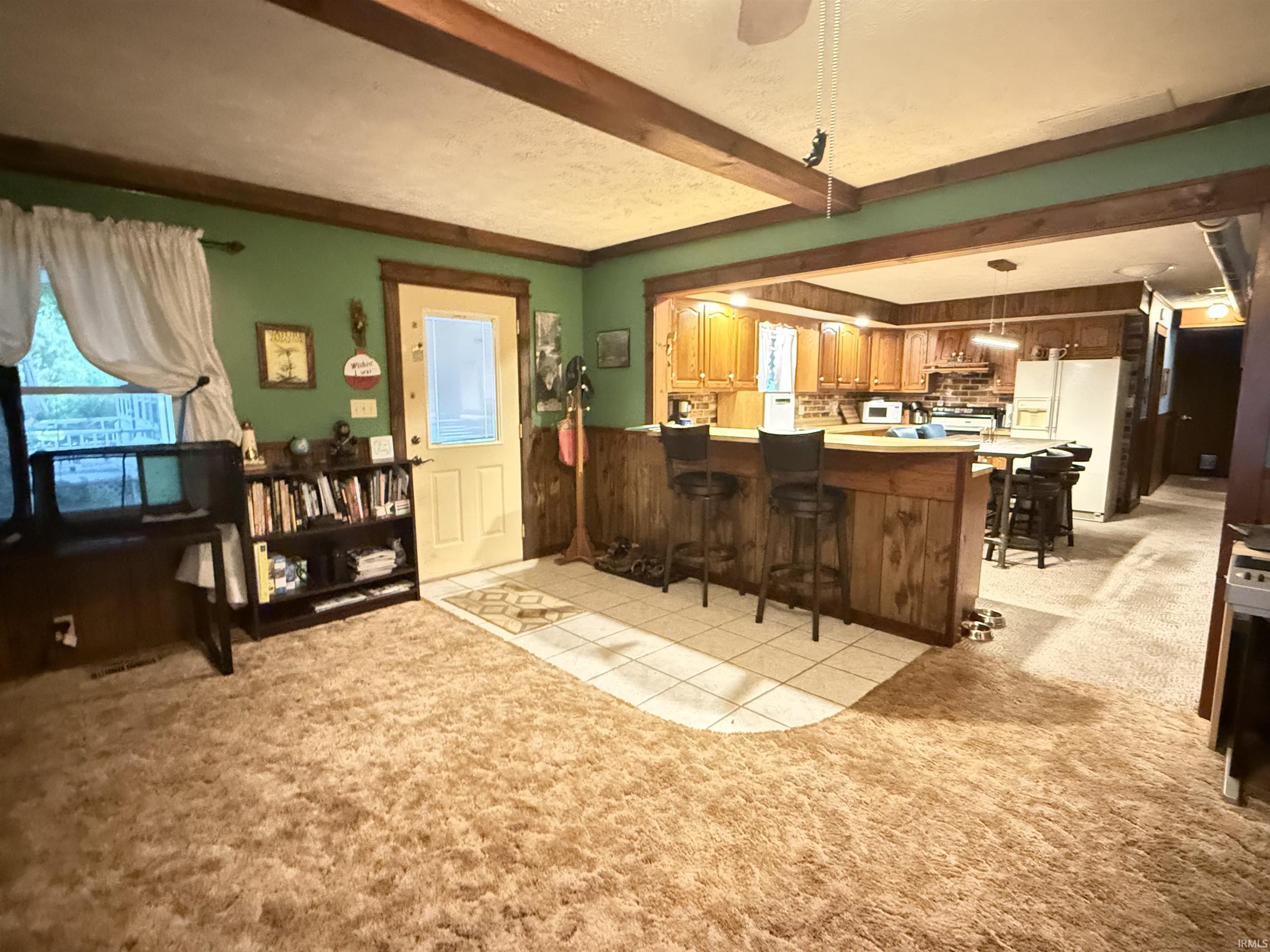 Exposed ceiling beams, wood-paneled breakfast bar, tile flooring, wood-finish cabinetry, and a bright window