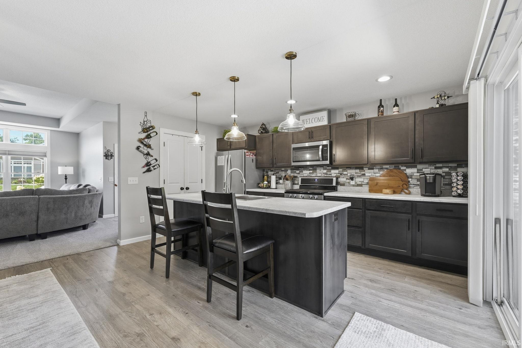 Kitchen featuring dark wood-finish cabinetry, stainless steel appliances, a tile backsplash, and an island with pendant lighting