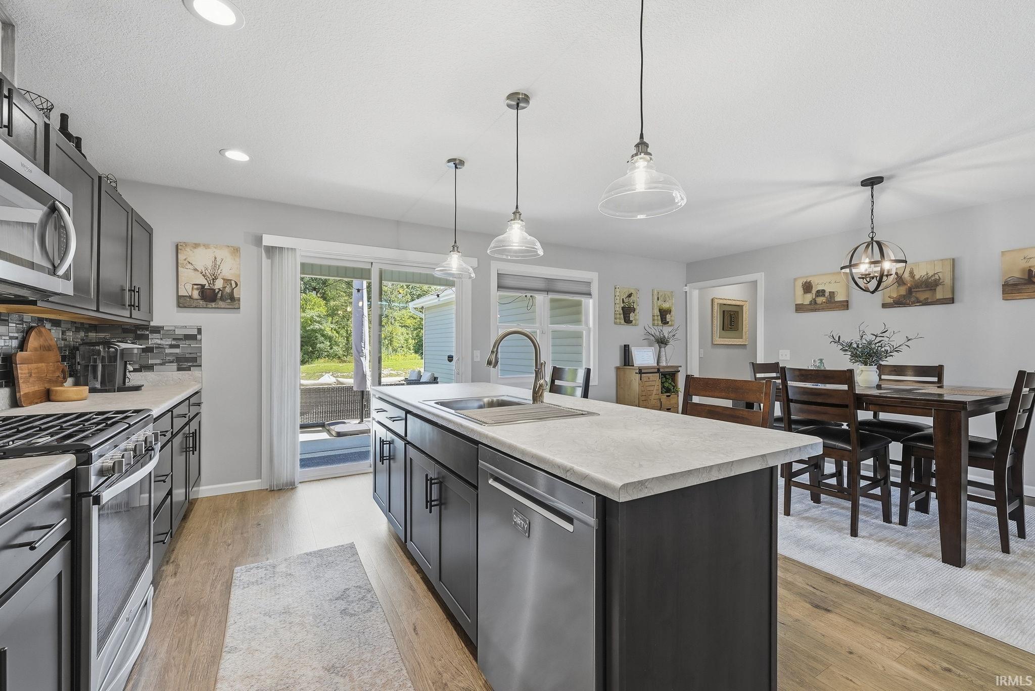 Kitchen featuring wood-finish flooring, dark cabinetry, light countertops, stainless steel appliances, and a mosaic tile backsplash