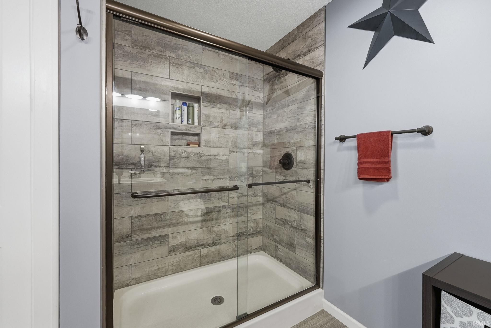 Shower enclosure with sliding glass door, textured tile surround, and dual recessed shelving