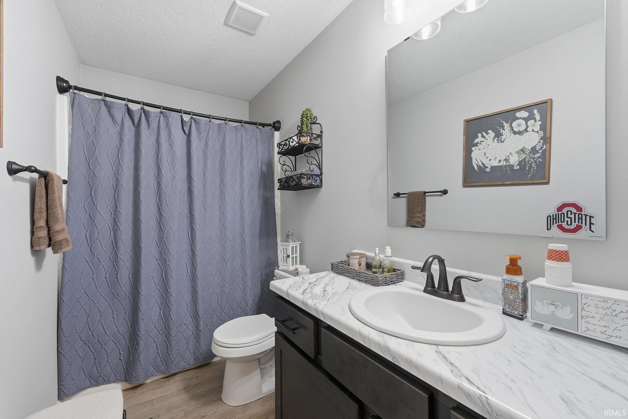 Spa-inspired bathroom featuring a curved vessel sink with quartz countertop, matte black faucet and hardware, dark cabinetry with storage, and a coordinating plumbing fixture package