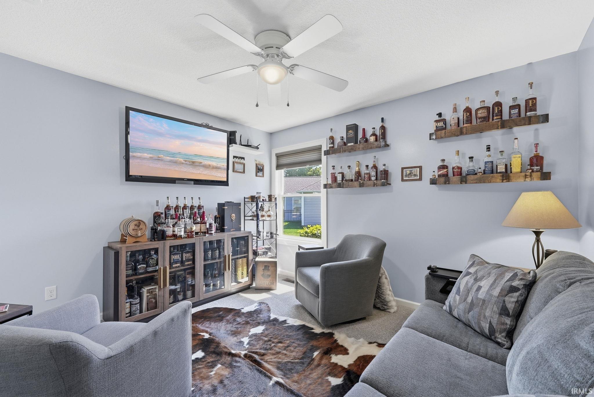 Ceiling fan with integrated lighting, wall-mounted shelving, built-in display cabinetry, and window with roller shade