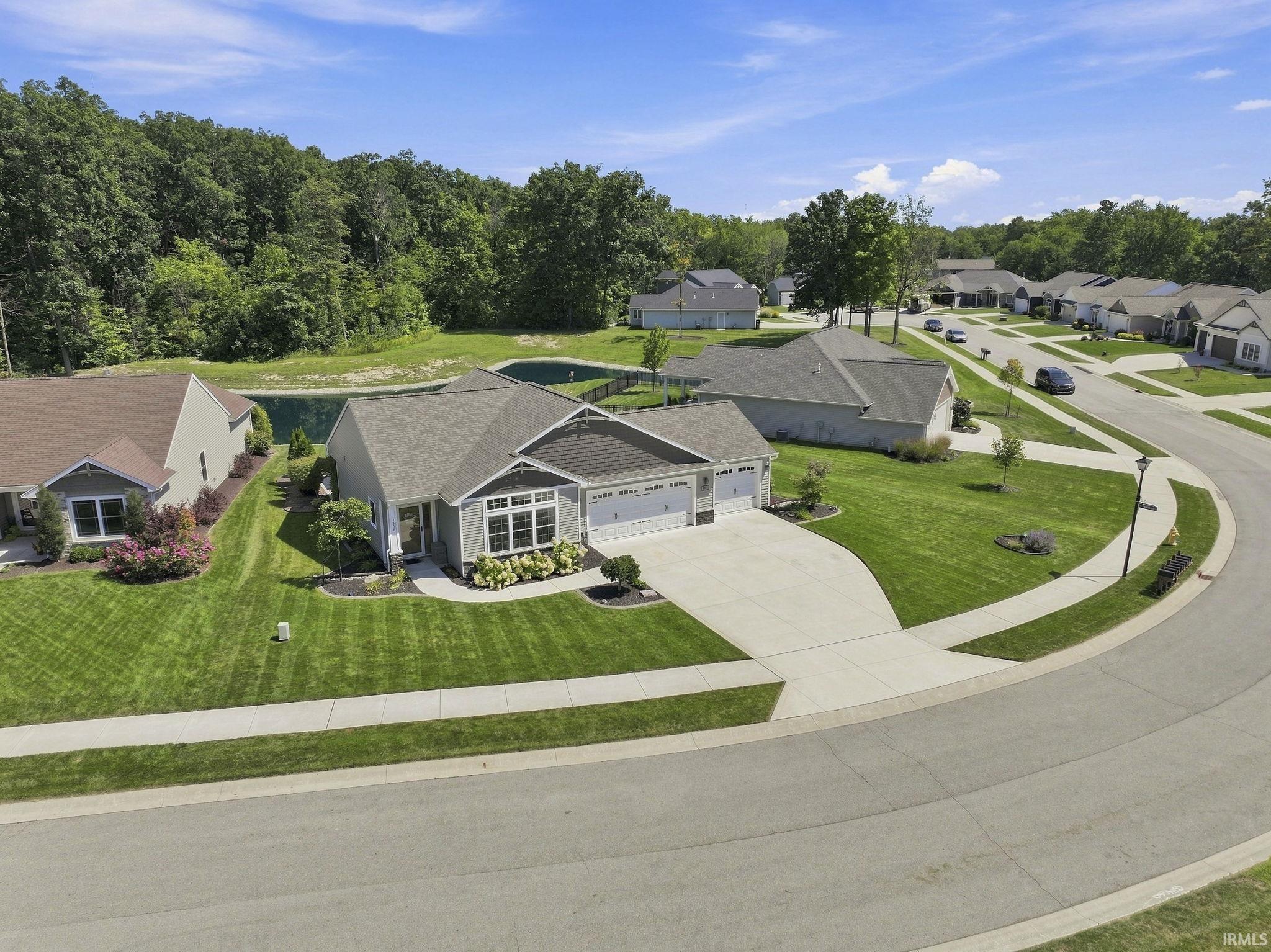 Single-story residence featuring a two-car garage, mature landscaping, and an adjacent water feature