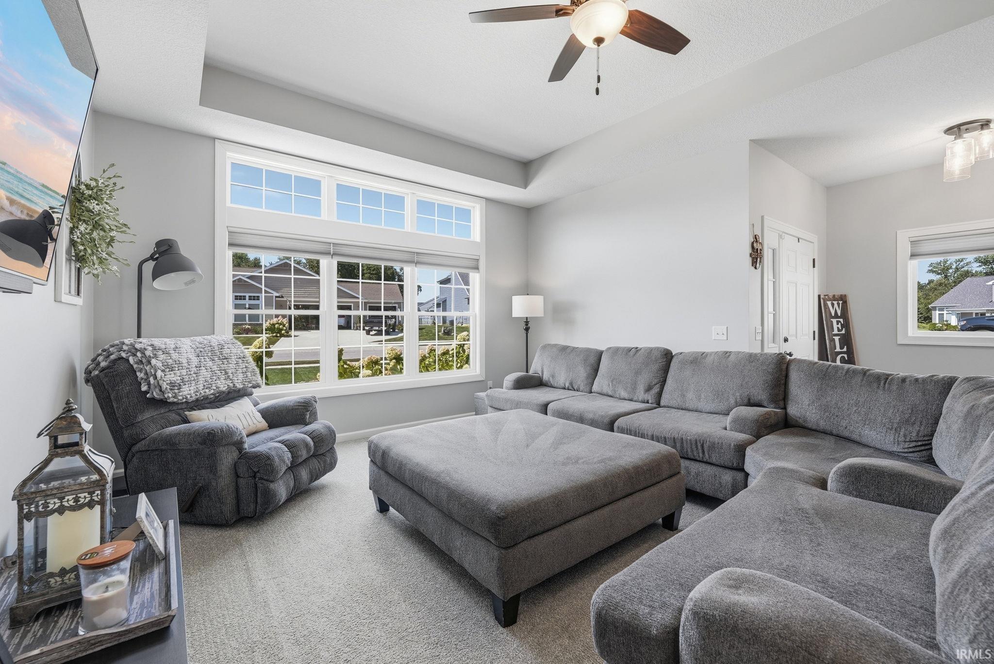 Great room featuring a vaulted ceiling, ceiling fan with integrated lighting, a large window array with transom windows, and neutral carpeting