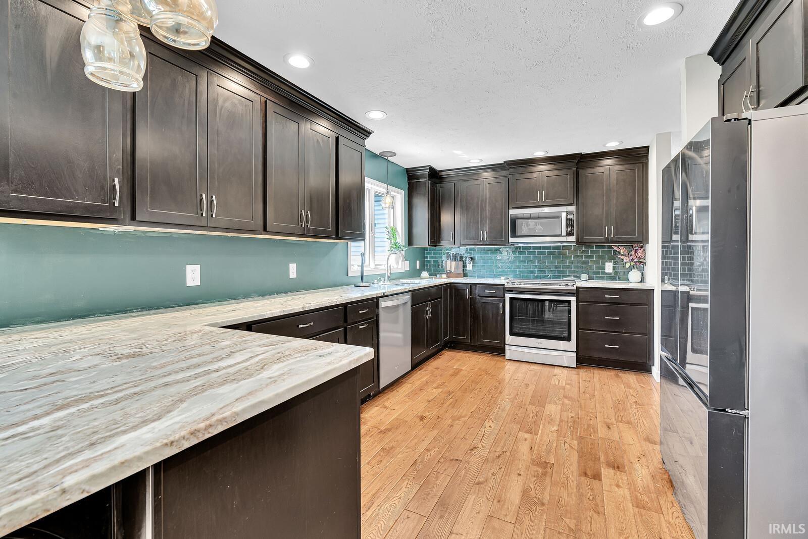 Hardwood flooring, dark wood cabinetry, white countertops, tile backsplash, and stainless steel appliances