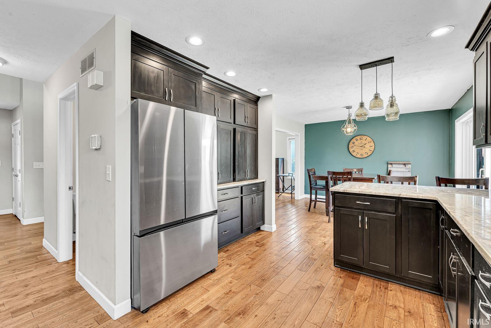 Wood-finish flooring, dark wood cabinetry, light-toned countertops, stainless steel refrigerator, and recessed lighting