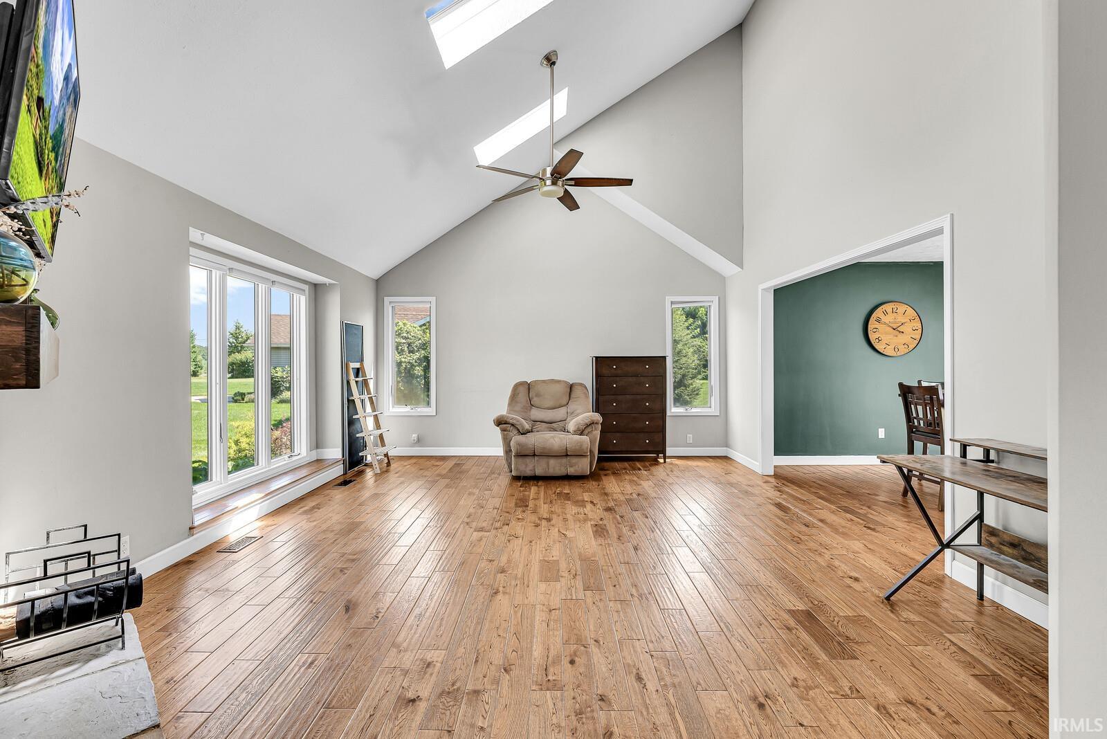 Vaulted ceiling with skylights, wood-finish flooring, ceiling fan, and large windows with integrated trim