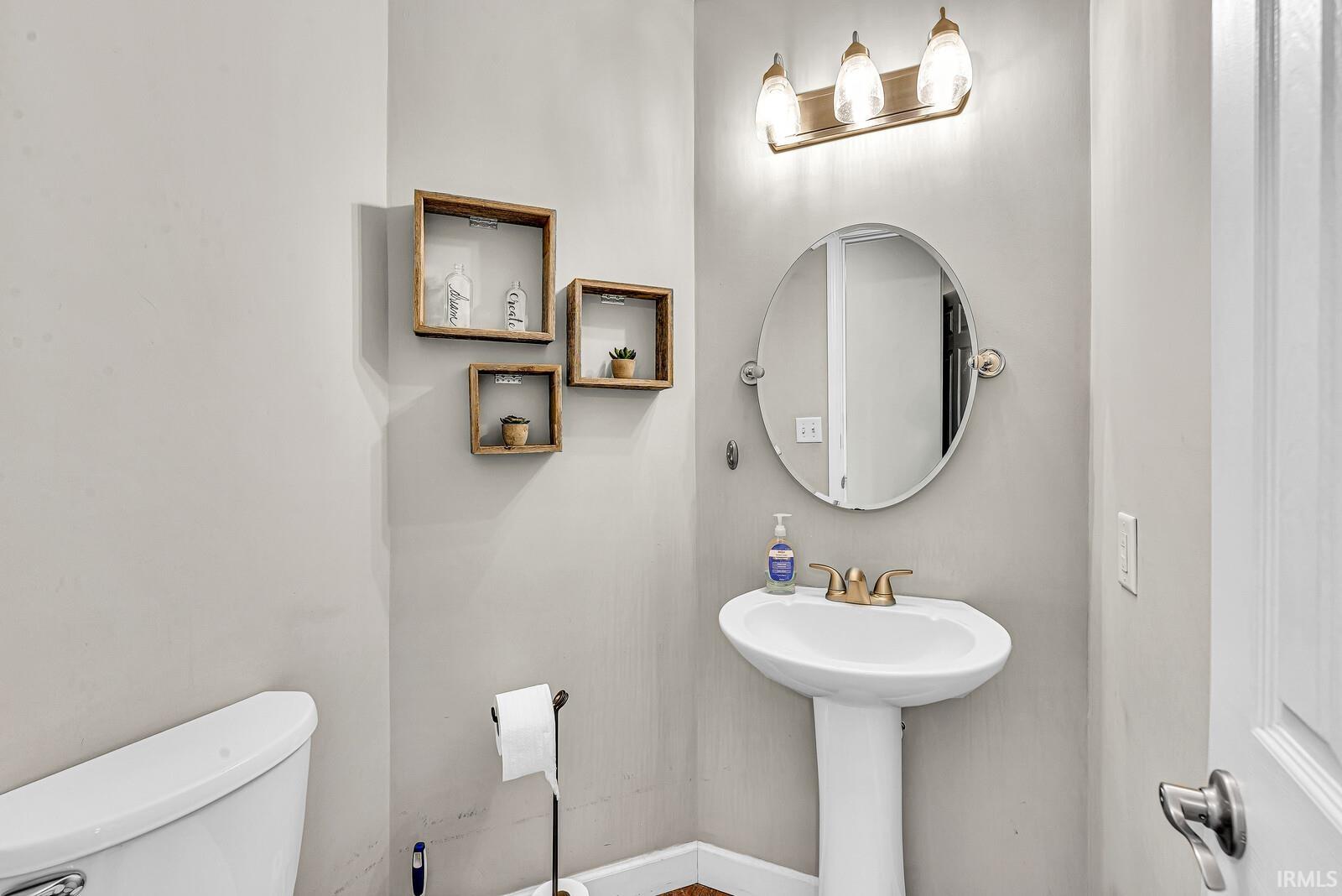 Pedestal sink with brass-finish faucet, circular mirror, and three-light vanity fixture