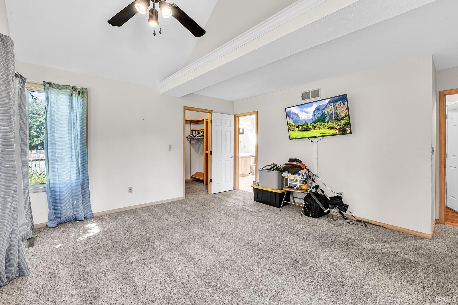 Neutral tone carpeting, a vaulted ceiling, and a ceiling fan with integrated lighting