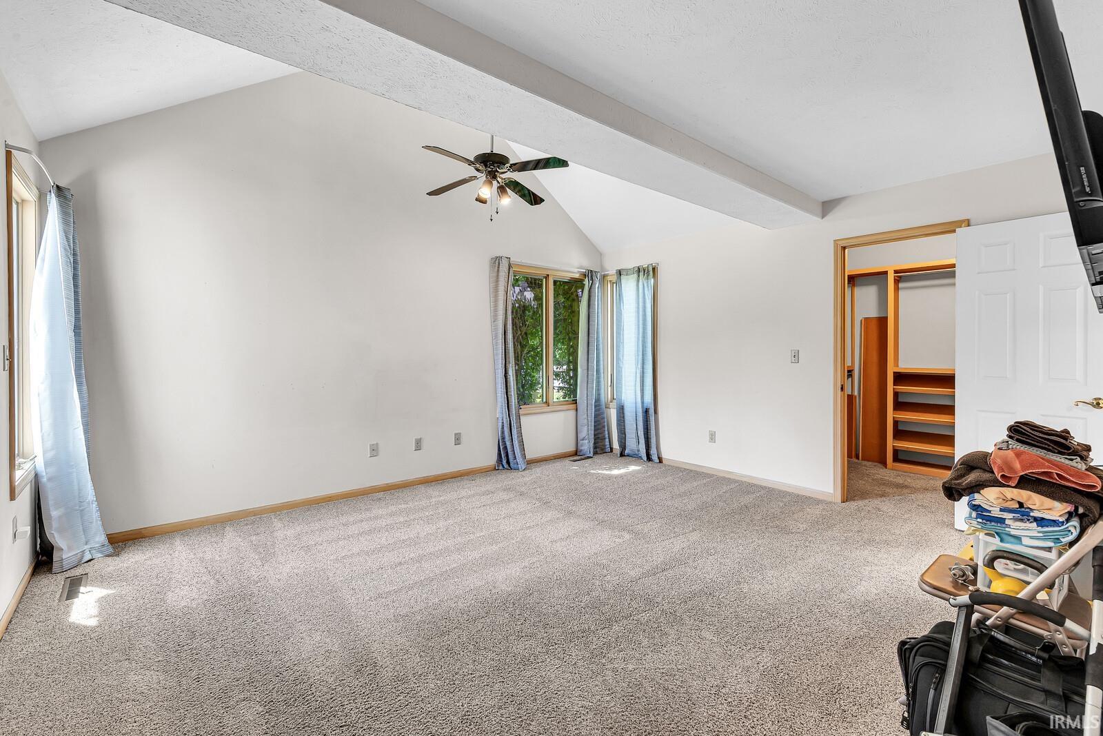 Vaulted ceiling, ceiling fan, carpet flooring, multiple windows, and built-in closet shelving