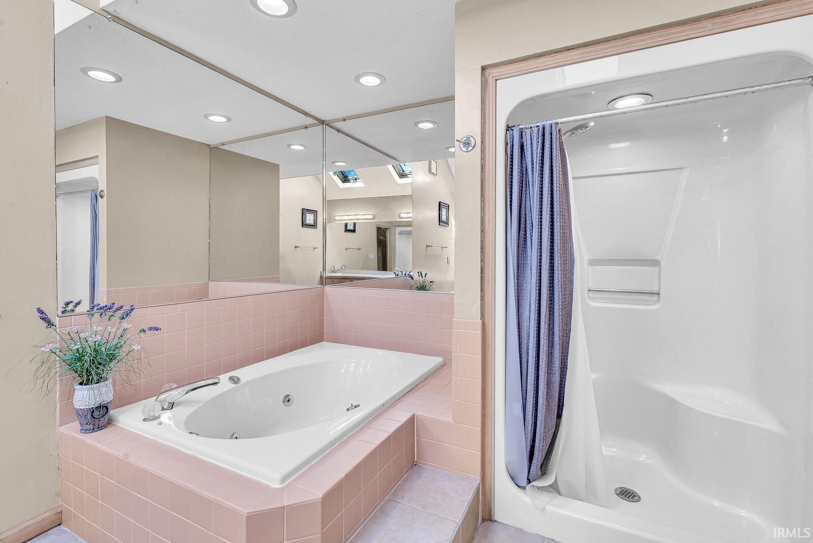 Built-in jetted tub surrounded by pink tile, recessed ceiling lighting, and a walk-in shower with a built-in seat