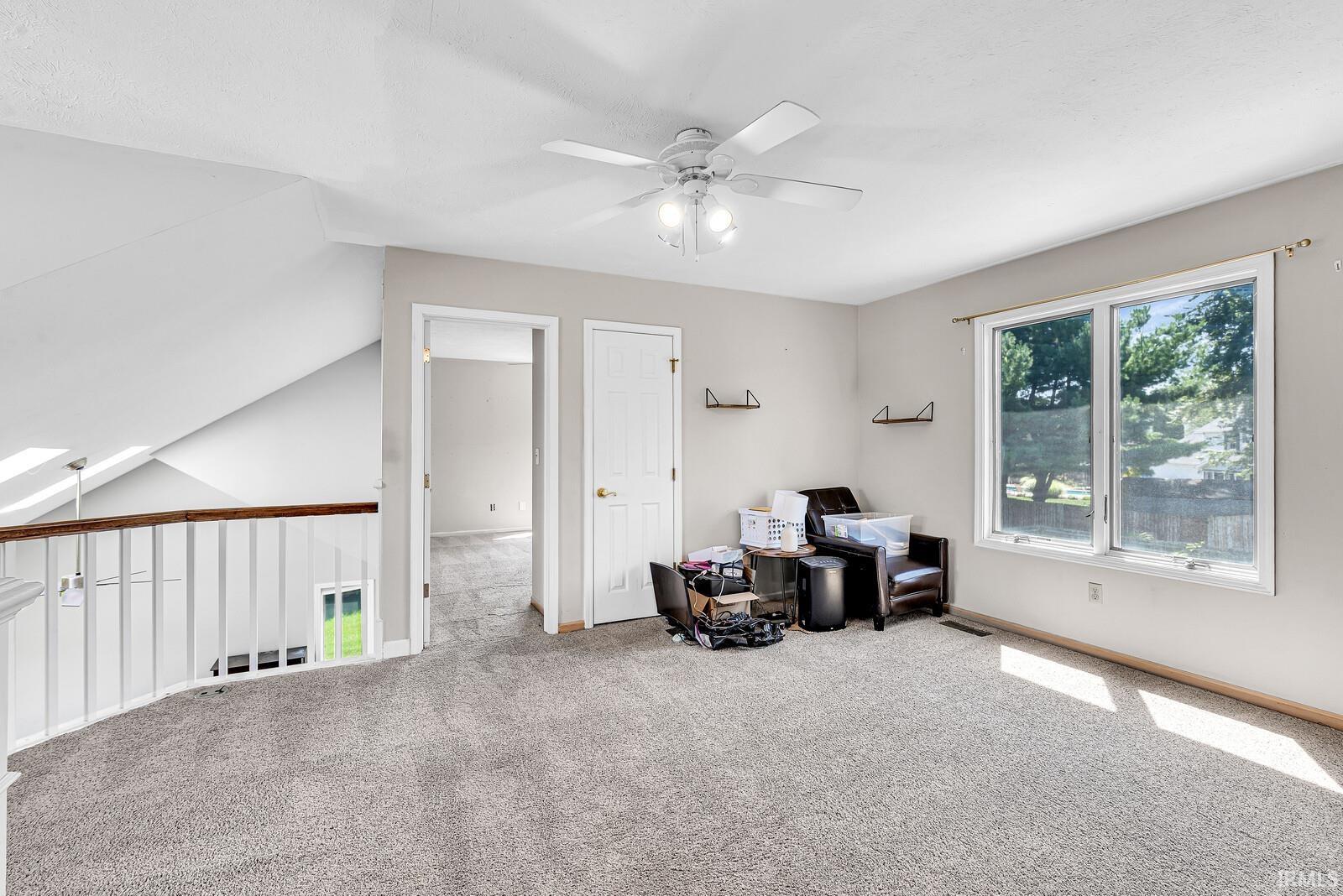 Carpeted flooring, white ceiling fan, ample natural light from multiple windows, white interior doors, and a white railing with a wood-finish top