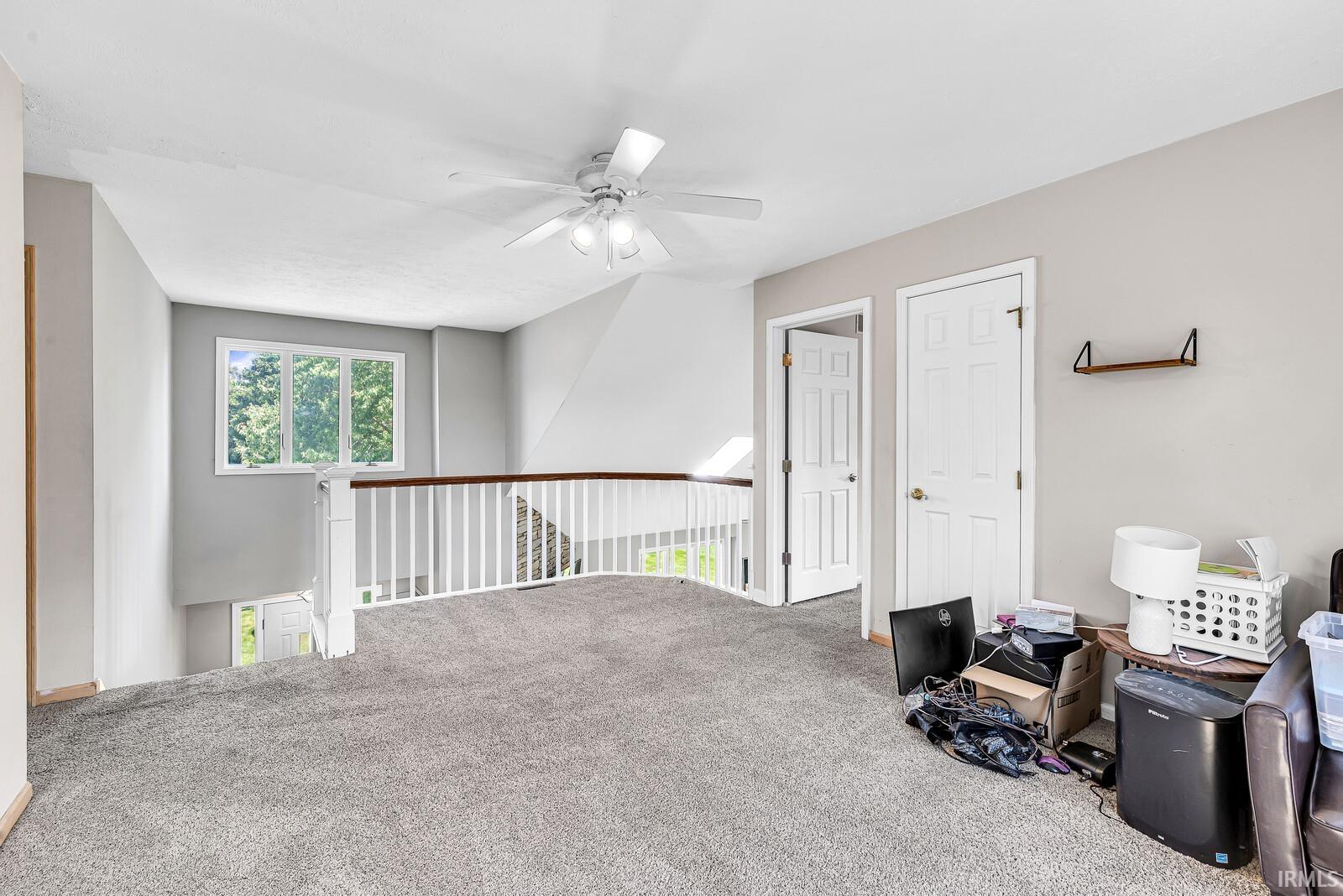 Carpeted loft area with a ceiling fan, white paneled doors, and a window with natural light