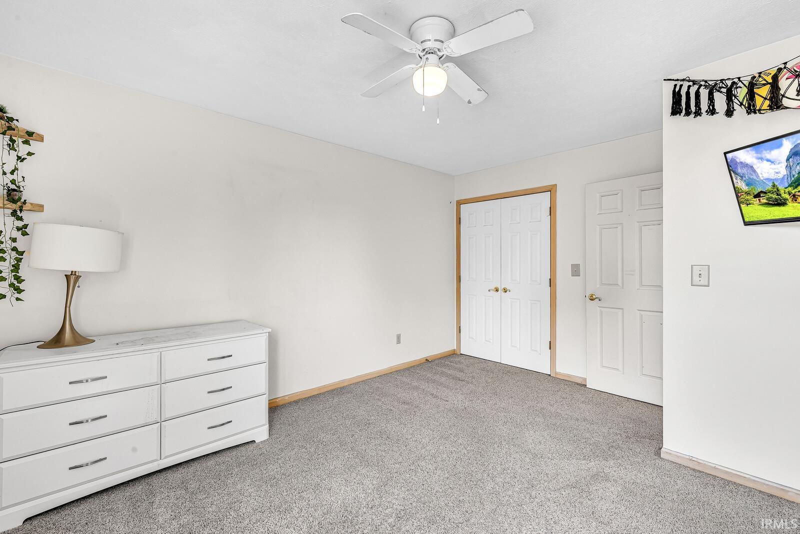 Neutral wall paint, textured carpeting, white ceiling fan with integrated lighting, and a white paneled door