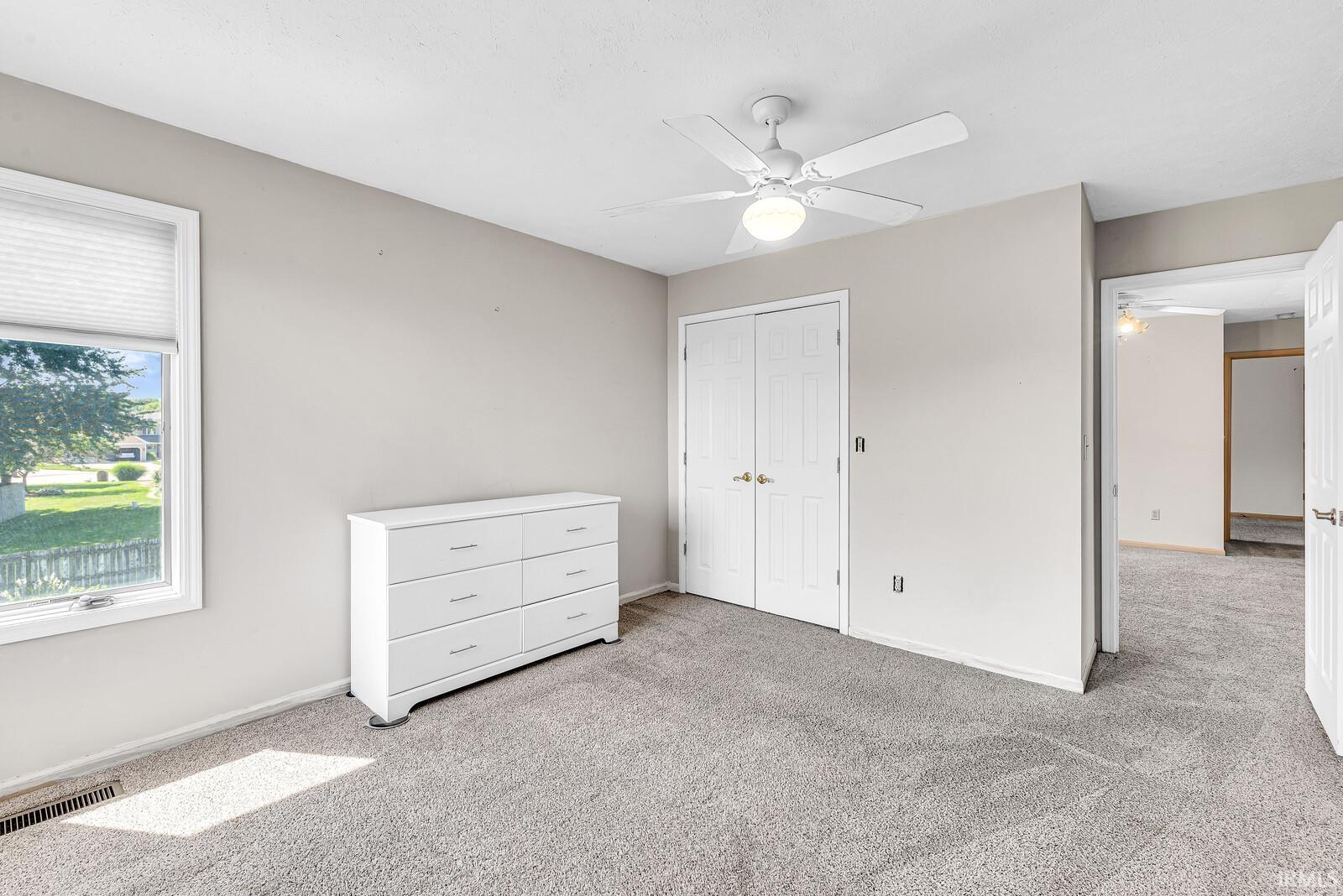 Neutral tone wall paint, light gray carpet flooring, ceiling fan with integrated lighting, white paneled double doors, and a window with blinds