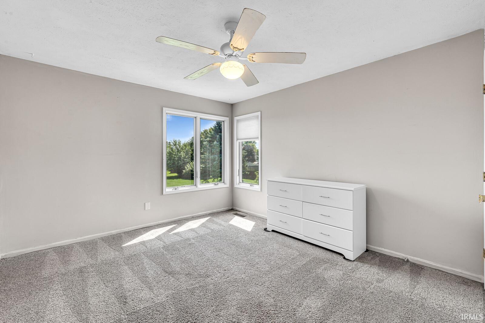Wall-to-wall carpeting, ceiling fan with integrated lighting, and multiple windows providing natural illumination