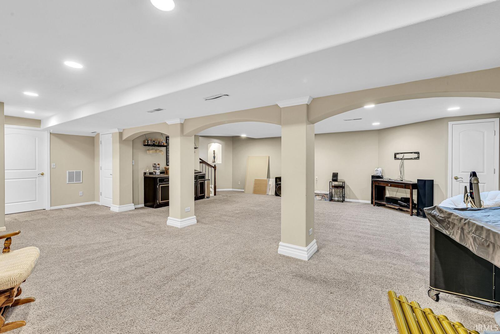 Expansive carpeted area with recessed lighting, architectural columns, and a built-in bar